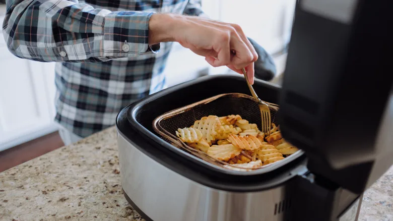Person flipping fries in an air fryer basket in a modern kitchen