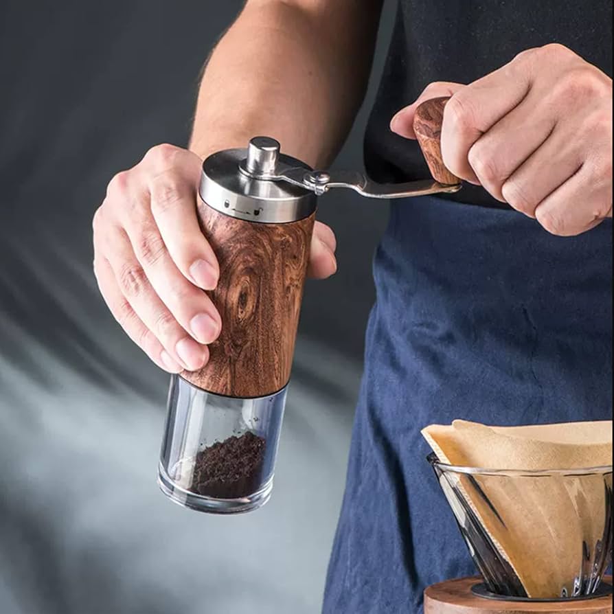 Person grinding coffee with a manual hand grinder next to a pour-over setup