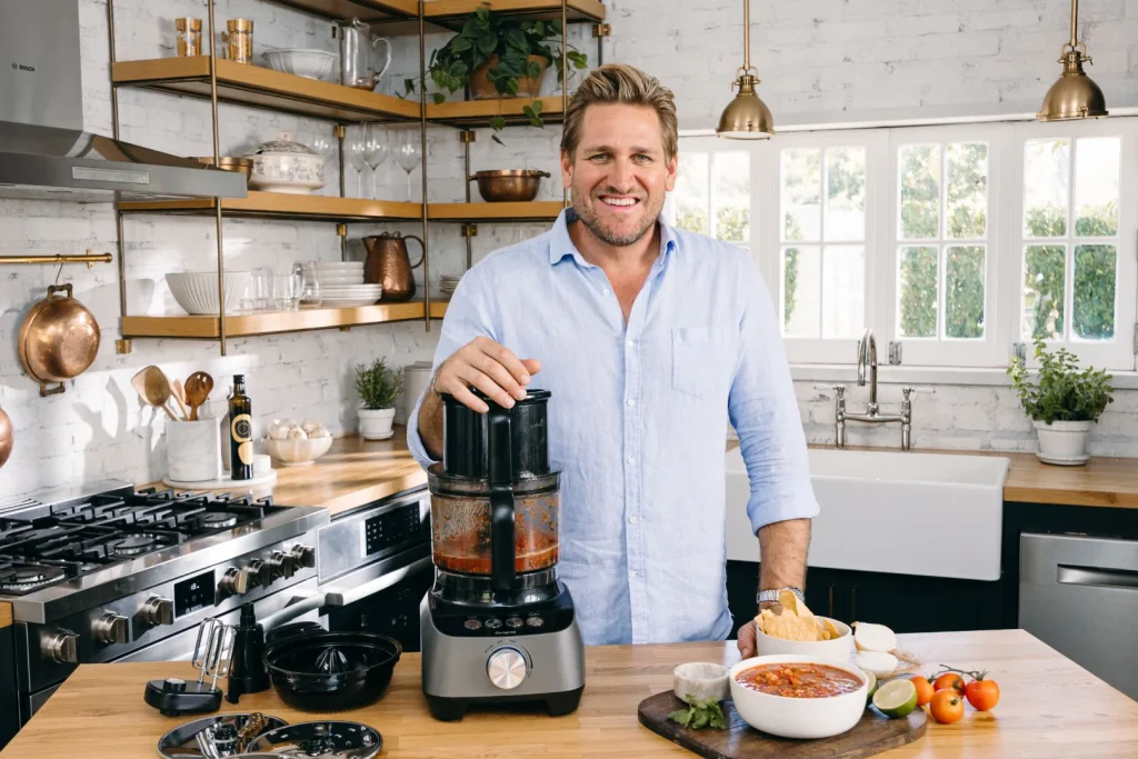 Modern food processor on a kitchen counter surrounded by fresh vegetables