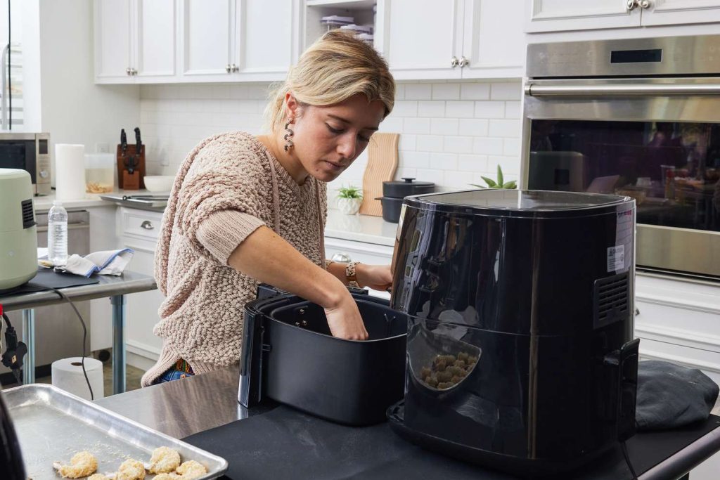 Woman preparing food in a large air fryer inside a modern kitchen — demonstrating proper appliance use.
