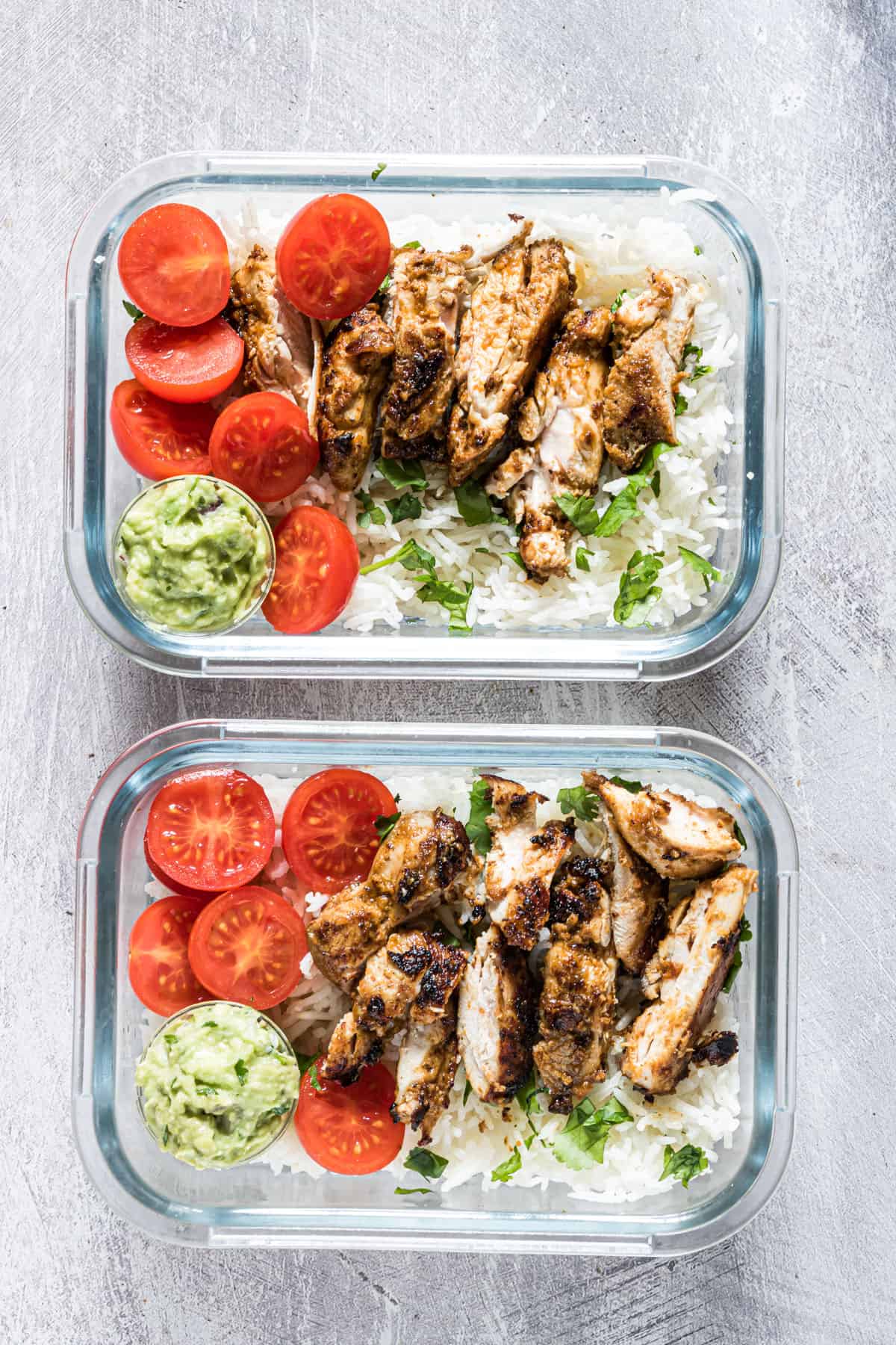 Chicken and rice meal prep bowls with cherry tomatoes and creamy avocado sauce.