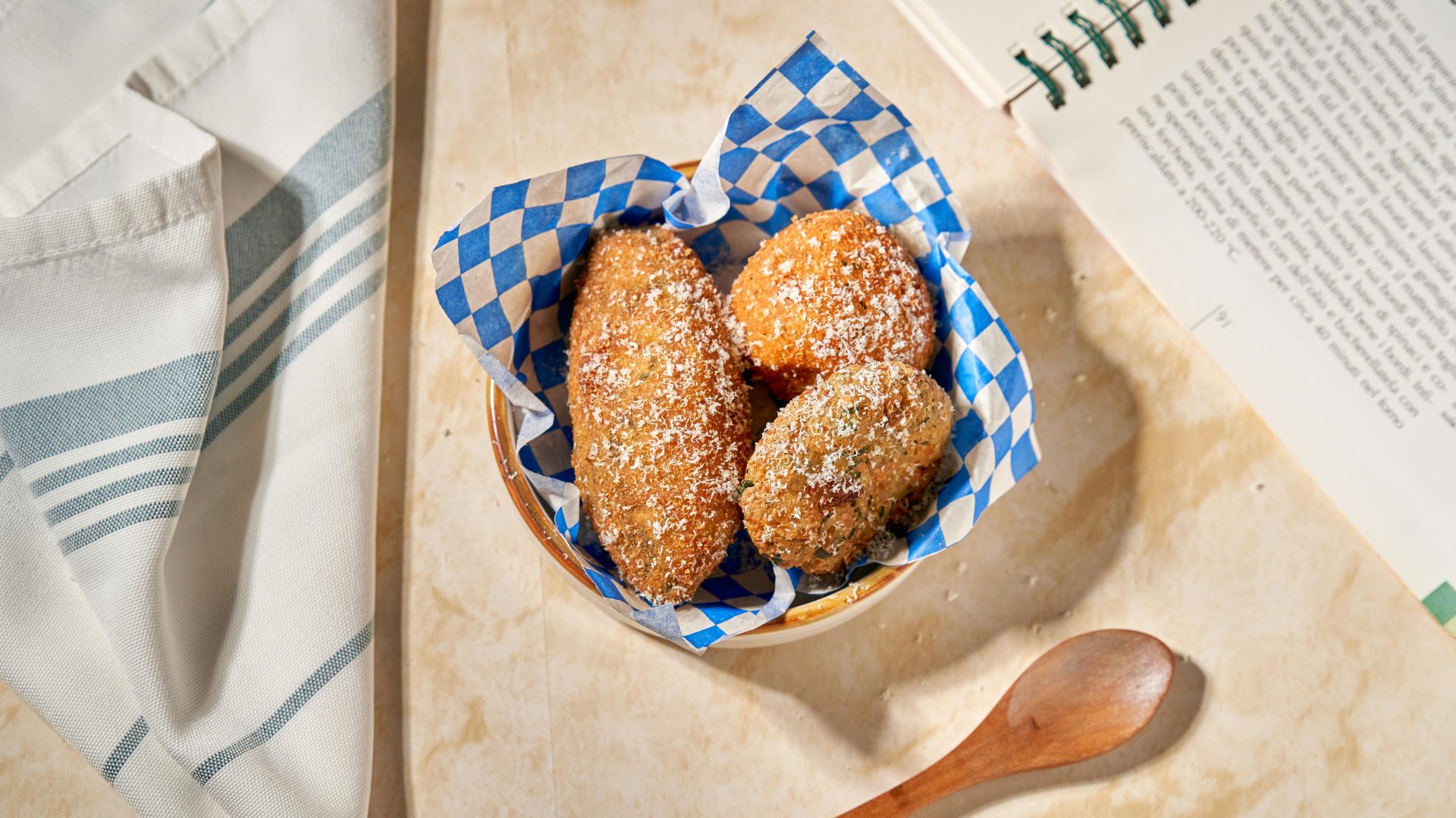 Crispy breaded snacks served in a basket with blue checkered paper, topped with grated cheese.