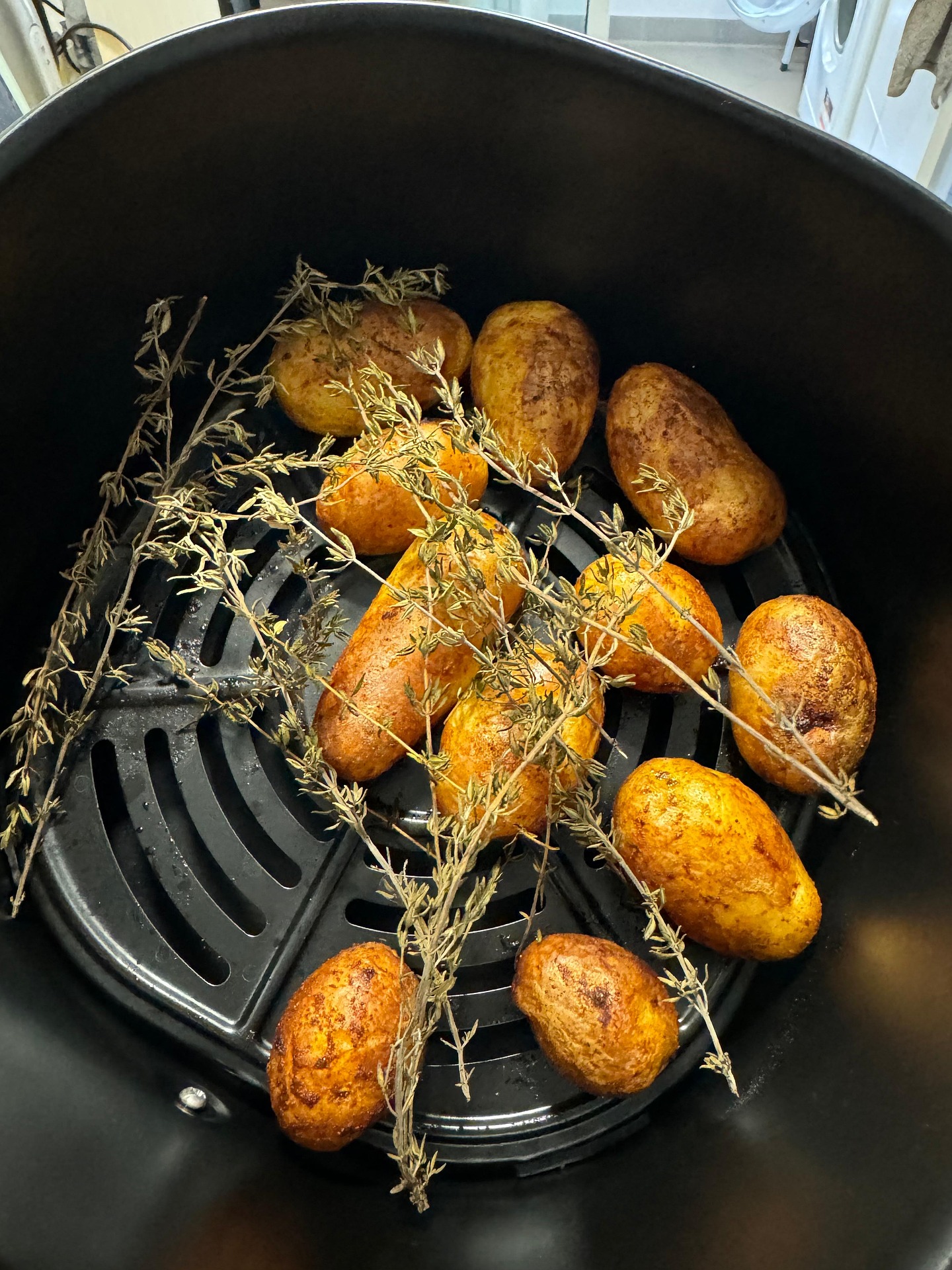 Golden roasted baby potatoes with herbs cooking inside an air fryer basket.