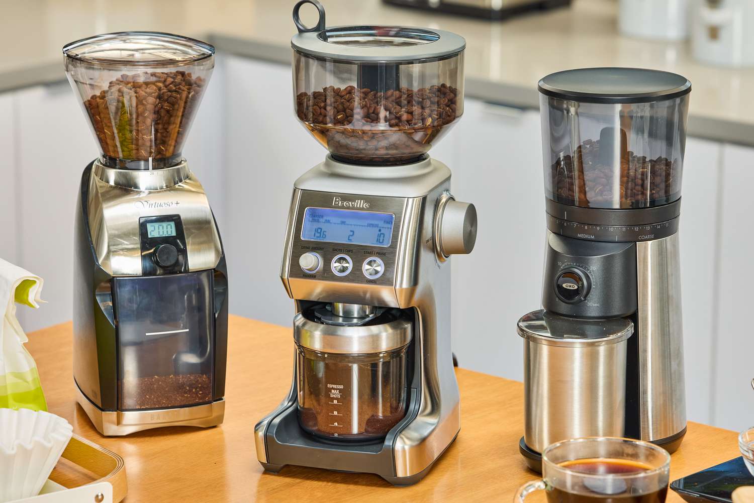 Three electric burr coffee grinders filled with beans on a kitchen counter