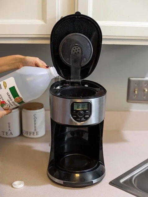 Pouring white vinegar into a coffee maker for descaling and cleaning