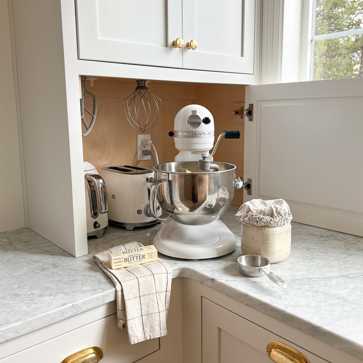 Stand mixer setup on a marble countertop with flour, butter, and baking tools in a bright modern kitchen.
