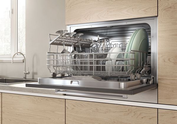 Compact dishwasher installed under a kitchen counter with neatly arranged dishes in a small modern kitchen