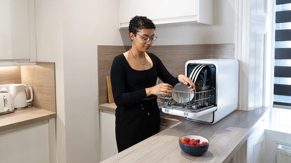 Woman loading dishes into a countertop dishwasher in a small apartment kitchen