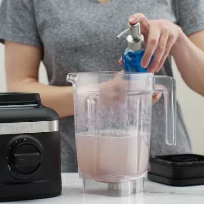 Person adding dish soap to a blender jar filled with water before running a cleaning cycle