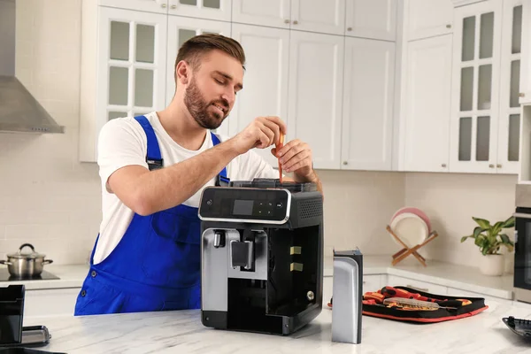repairman fixing a coffee maker with a screwdriver on a kitchen counter