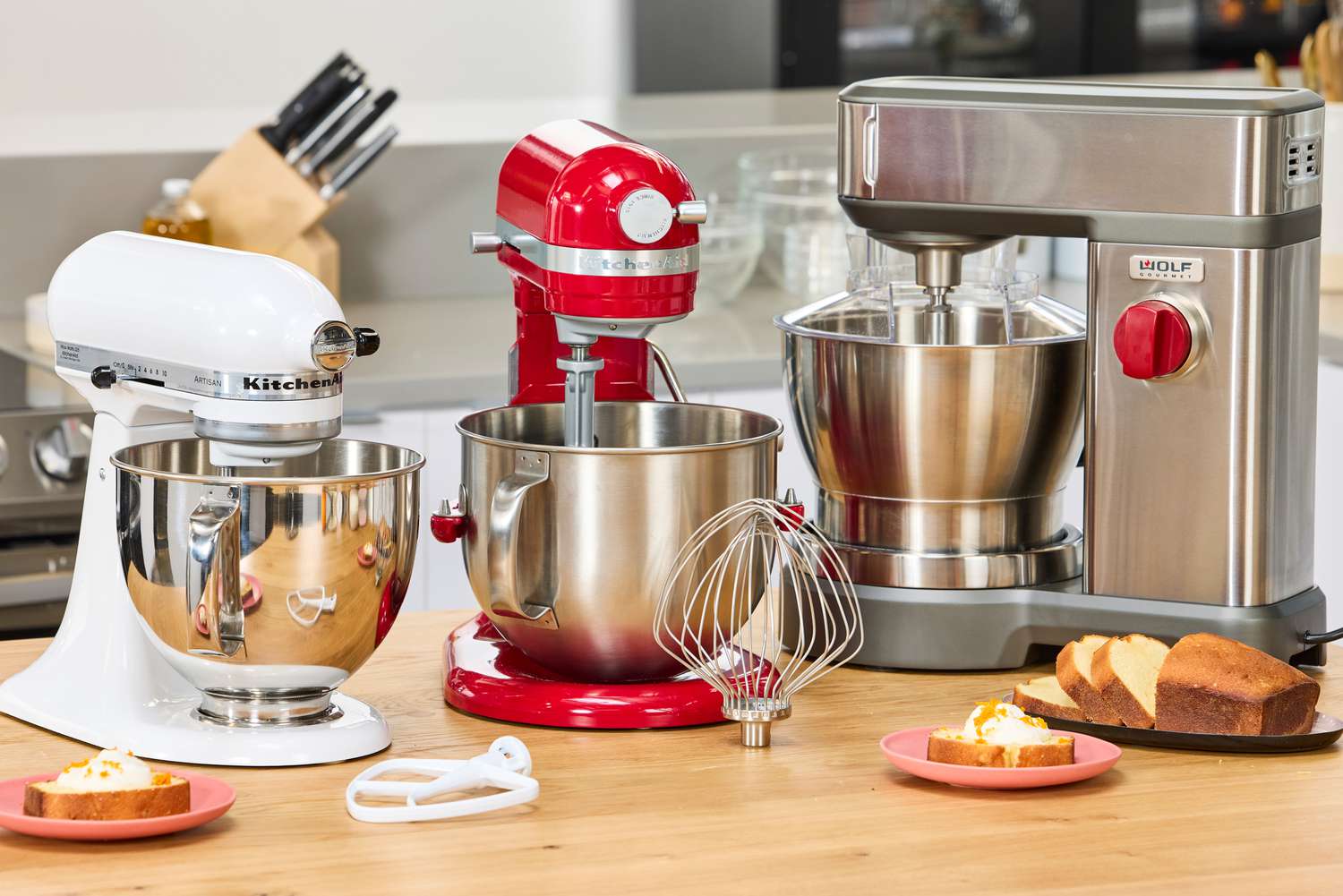 Budget-friendly stand mixers in different colors on a countertop with bowls, whisks, and baked loaf slices
