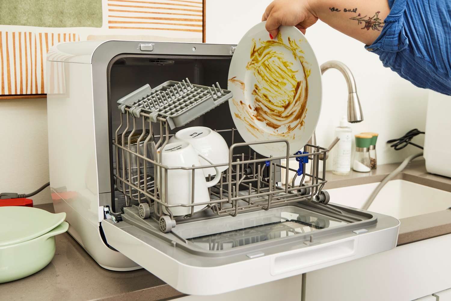 Countertop dishwasher loaded with dishes on a small kitchen counter in an apartment setting