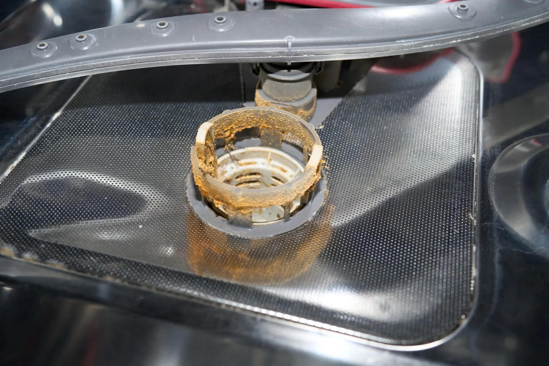 Close-up of a dishwasher drain opening with visible grease and food residue buildup restricting water flow