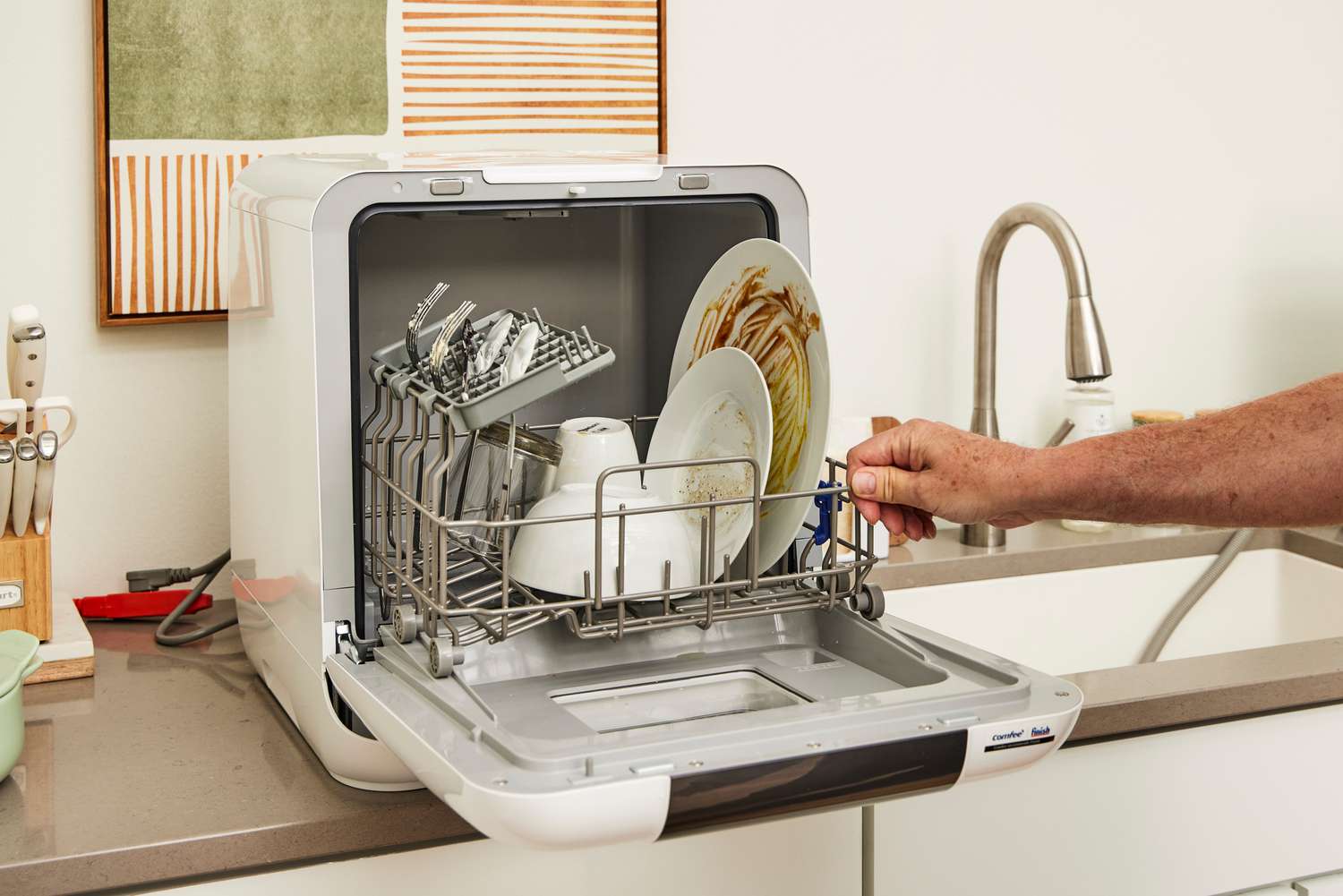 Countertop dishwasher installed beside a sink with door open and dishes loaded